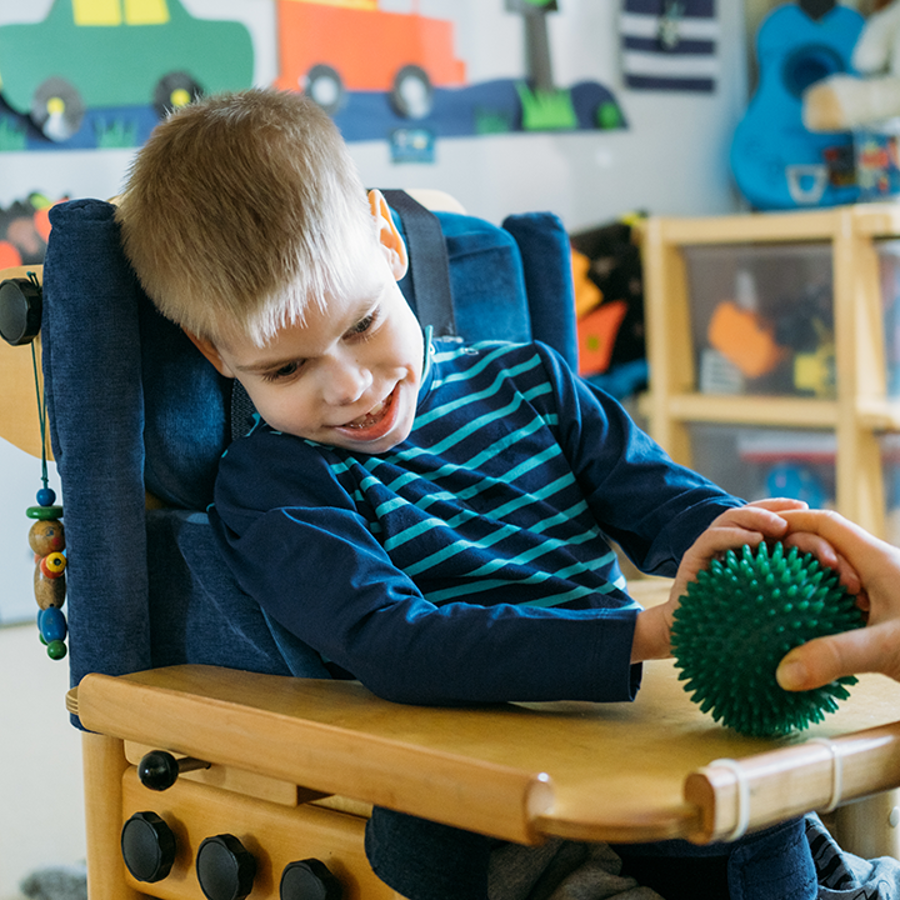 Boy In A Specialist Chair Playing With Plastic Spikey Massage Ball