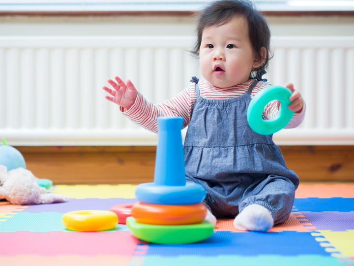 Baby girl sitting up on a playmat holding a toy in one hand