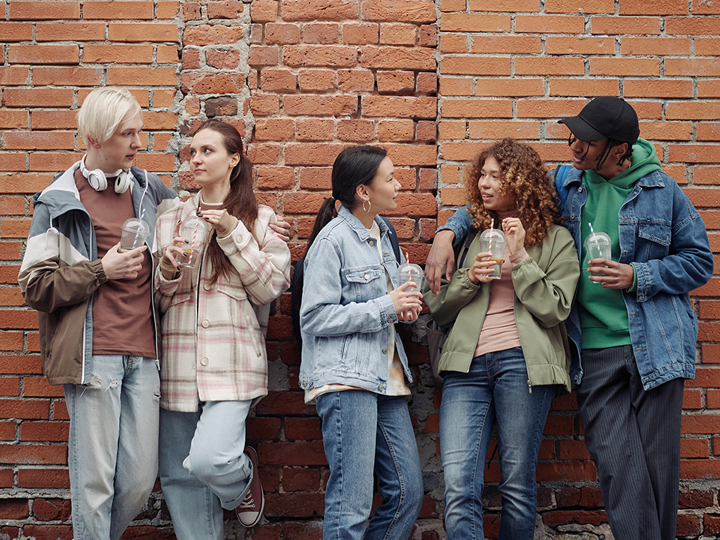 Group of 5 teenagers talking against a brick wall.