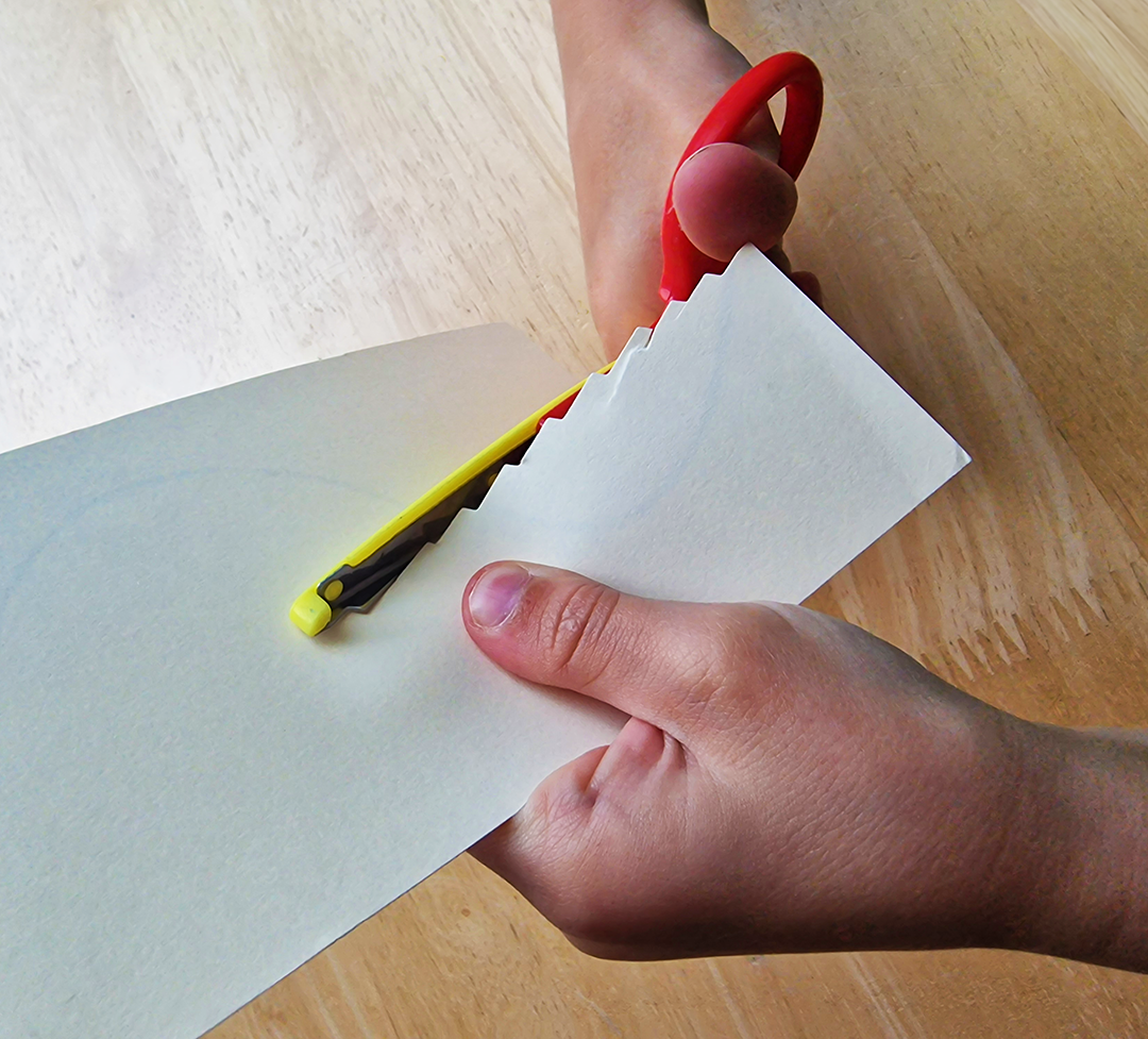 A child's hands using zigzag scissors on paper