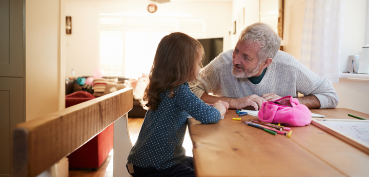 Grandad and granddaughter sitting at kitchen table colouring a picture and talking 