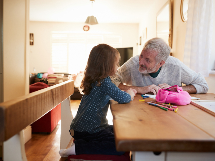 Grandad and granddaughter sitting at kitchen table colouring a picture and talking 