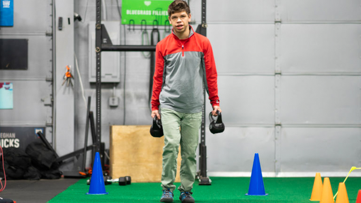 Disabled man doing kettlebell farmer lifts in gym