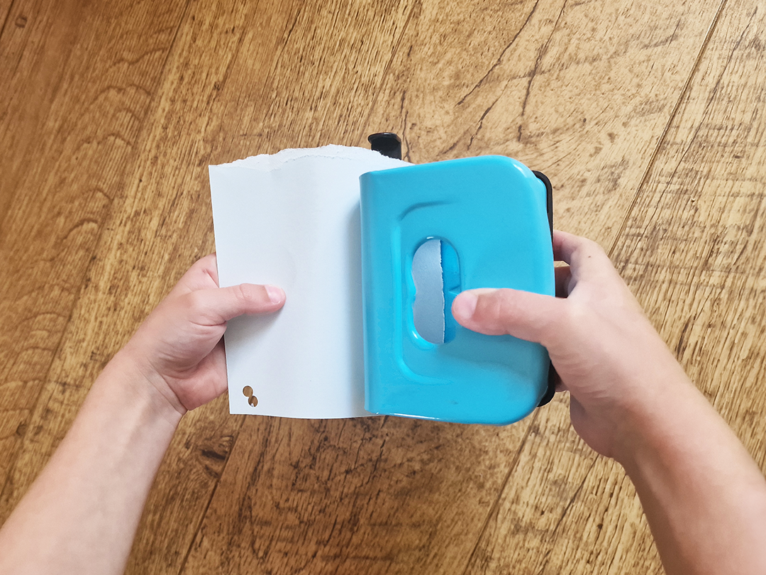 Child hands hole-punching paper using a blue holepuncher