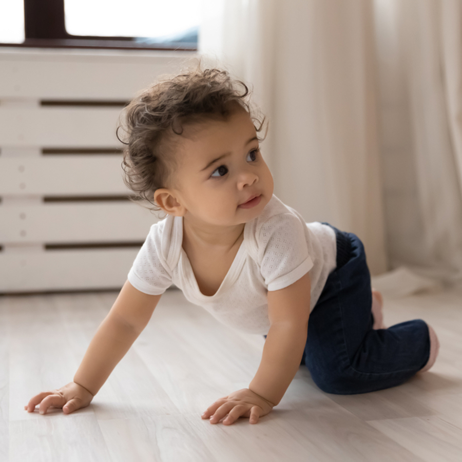 Baby crawling on their hands and knees across the floor.