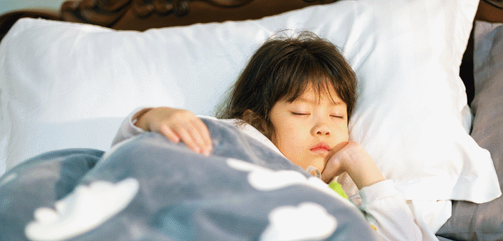 Young girl sleeping in bed with a blanket covered in clouds