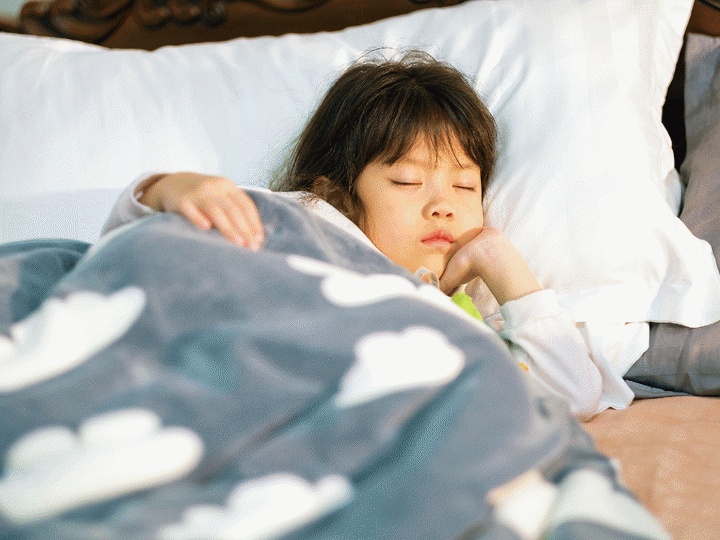 Young girl sleeping in bed with a blanket covered in clouds