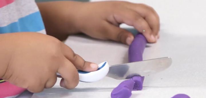 Young boy holding a knife cutting some playdough into pieces. 