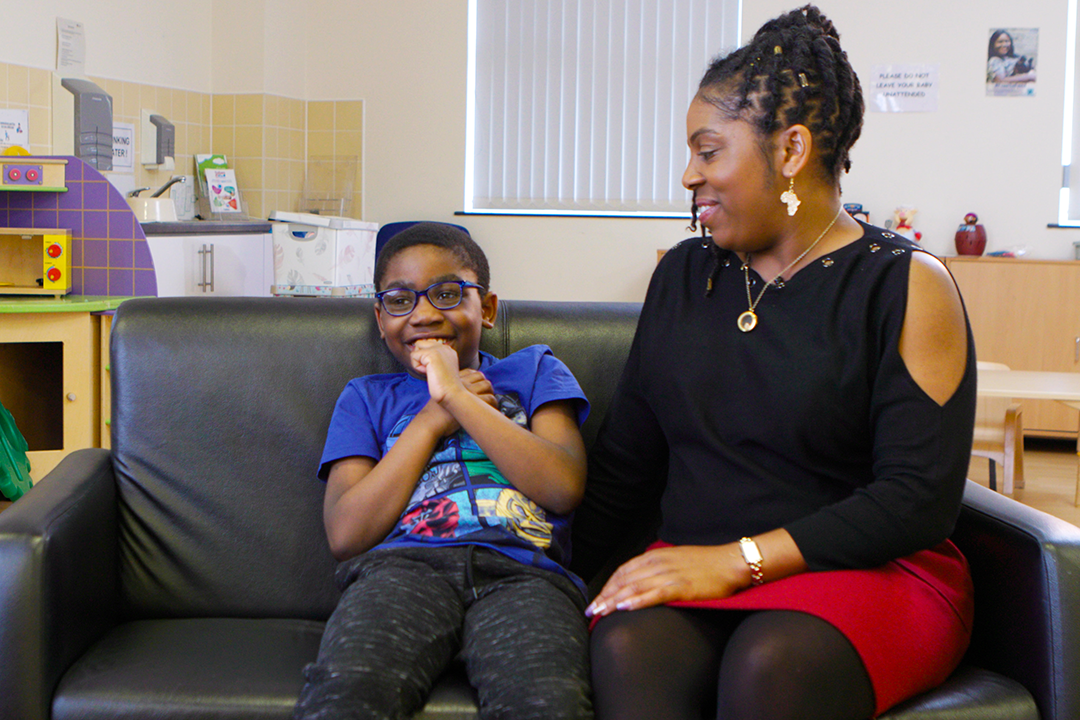 Excited child sitting on sofa next to their parent. Their parent is smiling at them.