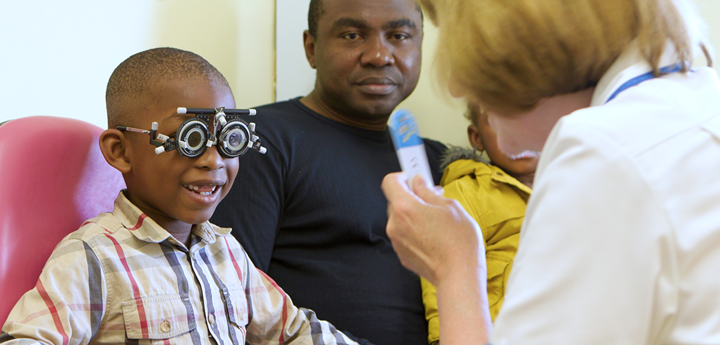 Boy sitting with parent, smiling whilst wearing glasses with adjustable lenses.