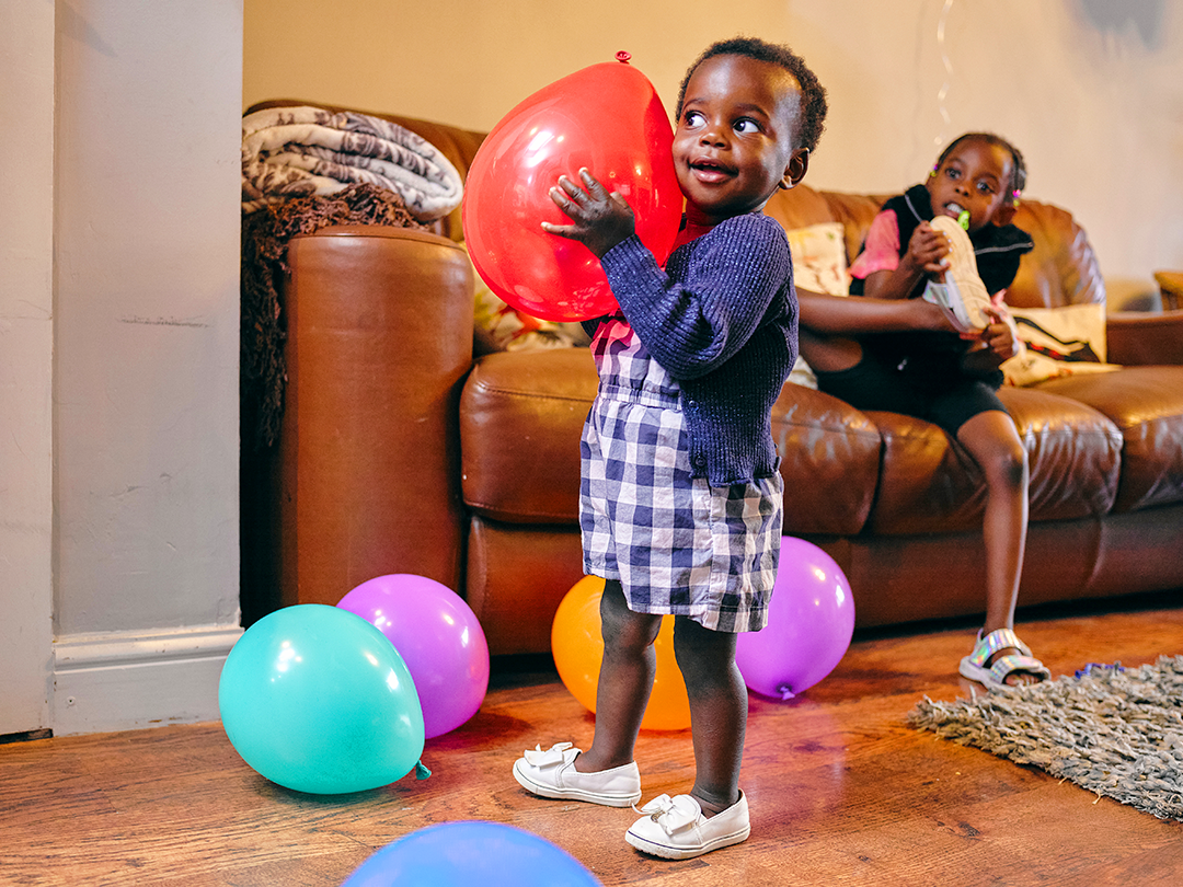 Child smiling holding a balloon in a living room.