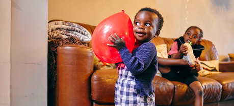 Child smiling holding a balloon in a living room.