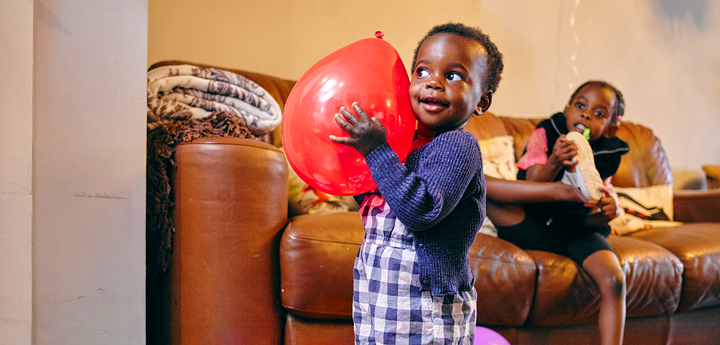 Child smiling holding a balloon in a living room.