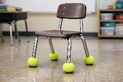 A classroom chair with tennis balls on each of the 4 legs