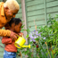 adult and child using a bright yellow watering can to water a plant outside