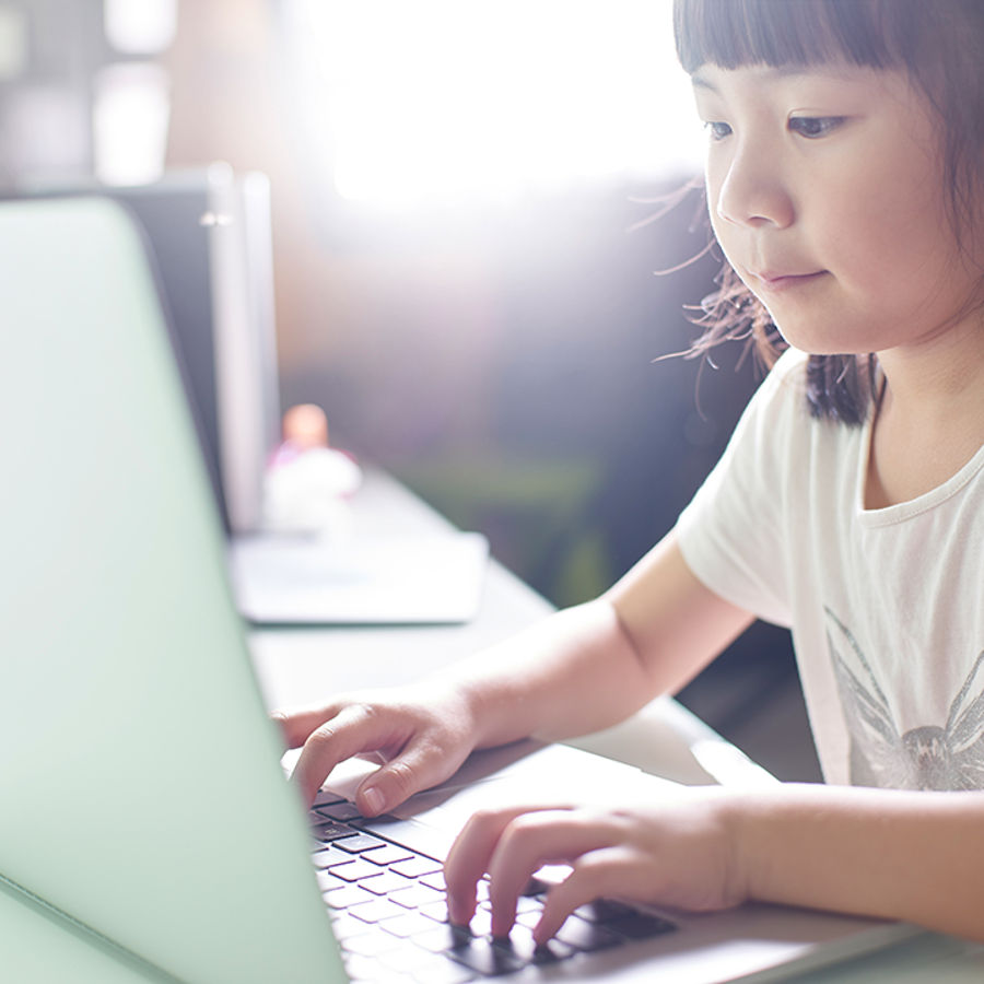 Young girl sitting at a table pressing keys on a laptop.