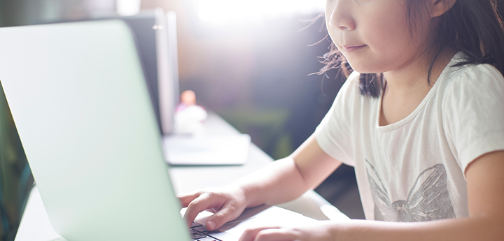 Young girl sitting at a table pressing keys on a laptop.