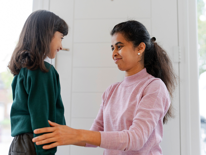 Adult kneeling, holding a child's arms. Both child and adult are smiling.