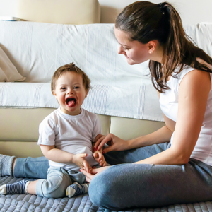 Young boy with Down's syndrome sitting on the floor with adult woman sitting next to him and gently holding his hands.