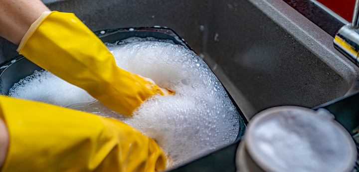 Washing up dishes in a sink with yellow gloves on.