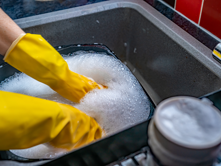 Washing up dishes in a sink with yellow gloves on.