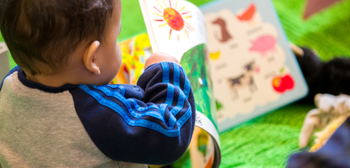 Boy toddler sitting on the floor holding a book and turning the page