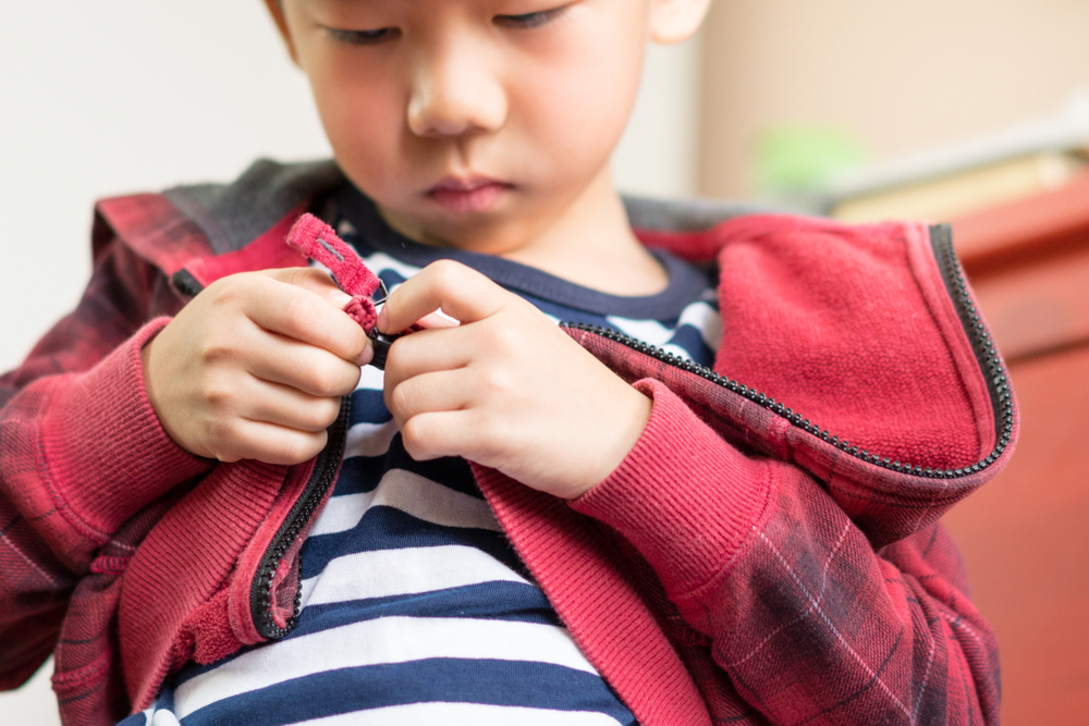 Child focusing on zipping a zipper on a hoodie.