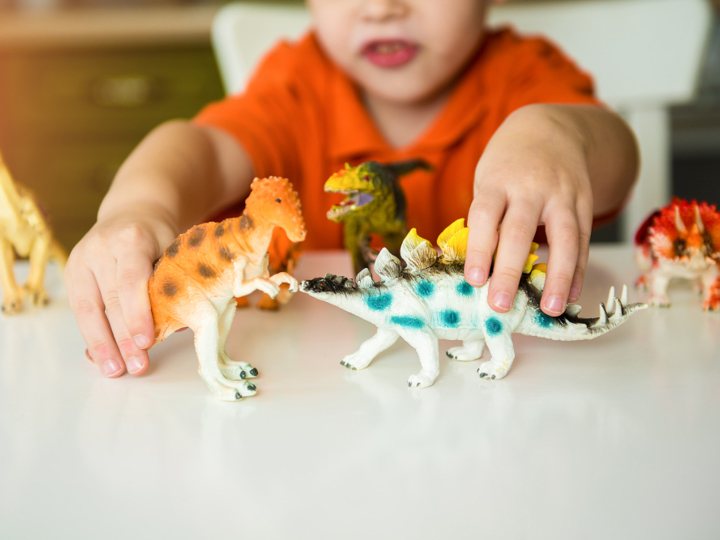 Boy in background holding 2 dinosaurs and playing with them together