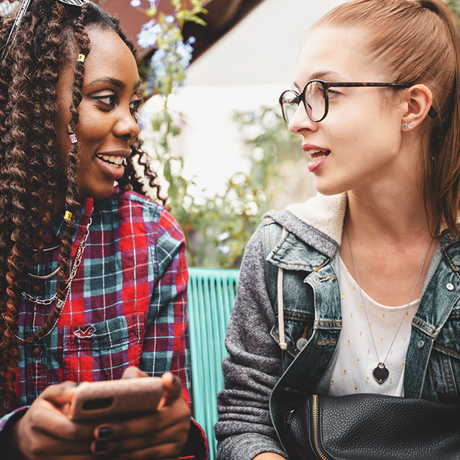 2 teenage girls talking. Girl on left is holding a phone