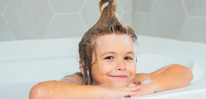 A child in the bath. Their hair is washed and pulled into a giant curl on the top of their head.