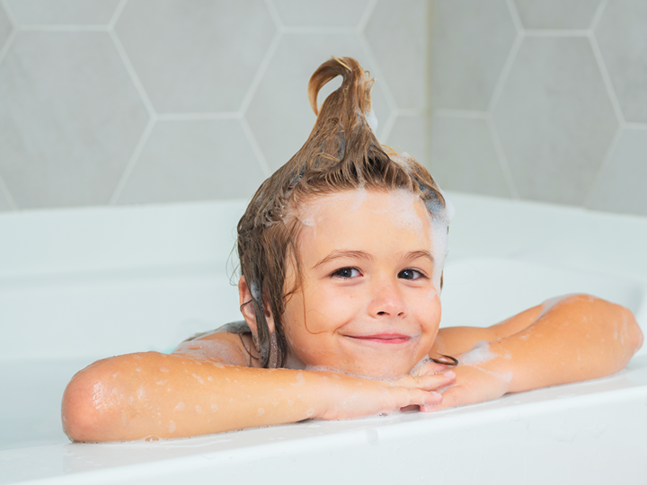 A child in the bath. Their hair is washed and pulled into a giant curl on the top of their head.