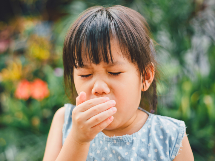 Girl coughing into her hand in a garden