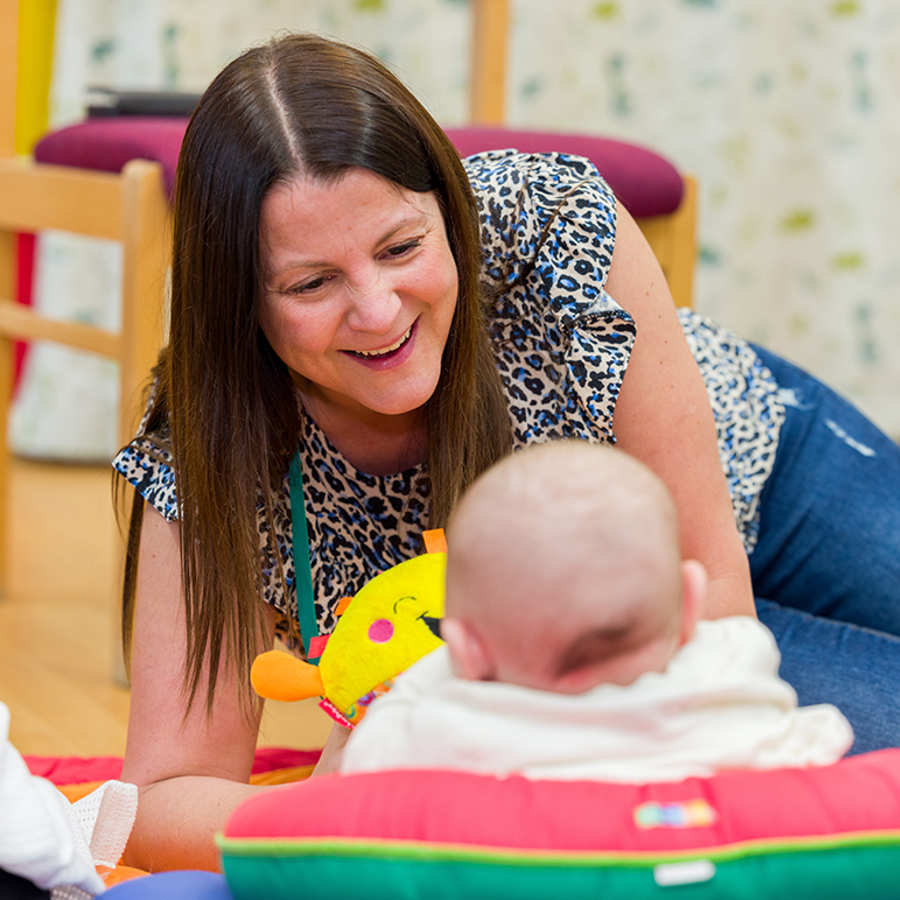 smiling adult woman playing with a baby on the floor