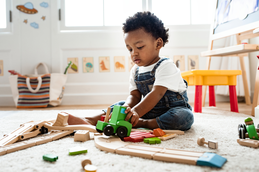 Toddler sitting on the floor in a playroom playing with wooden toys 