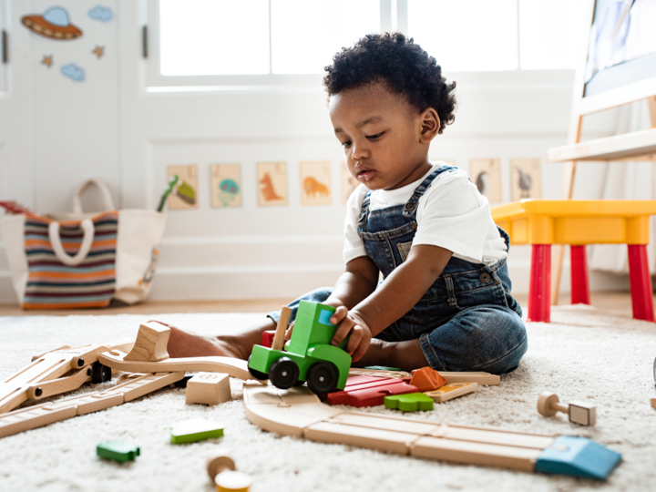 Toddler sitting on the floor in a playroom playing with wooden toys 