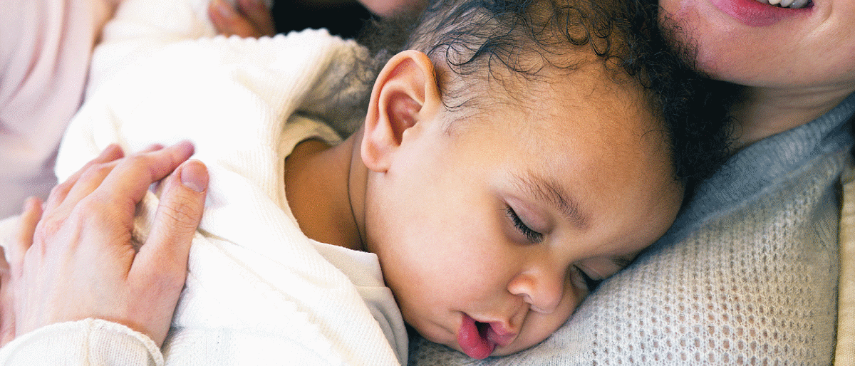 Baby sleeping on woman's chest. Their head is turned towards the camera.