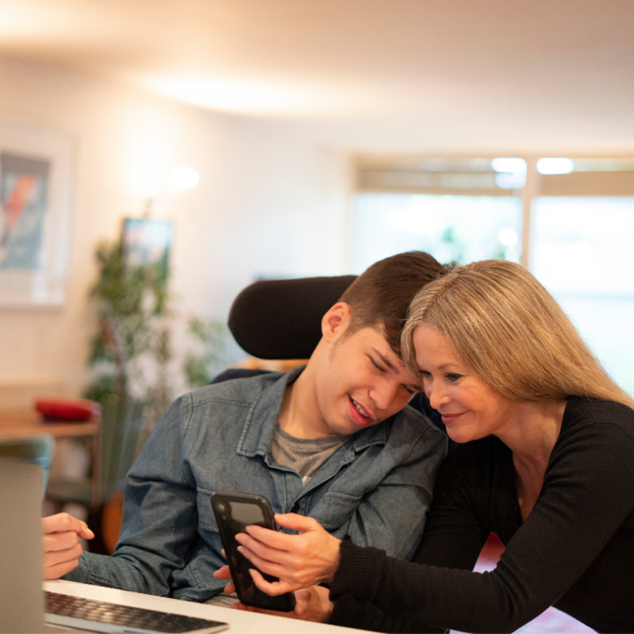 Disabled Young Adult Looking At Phone With Adult