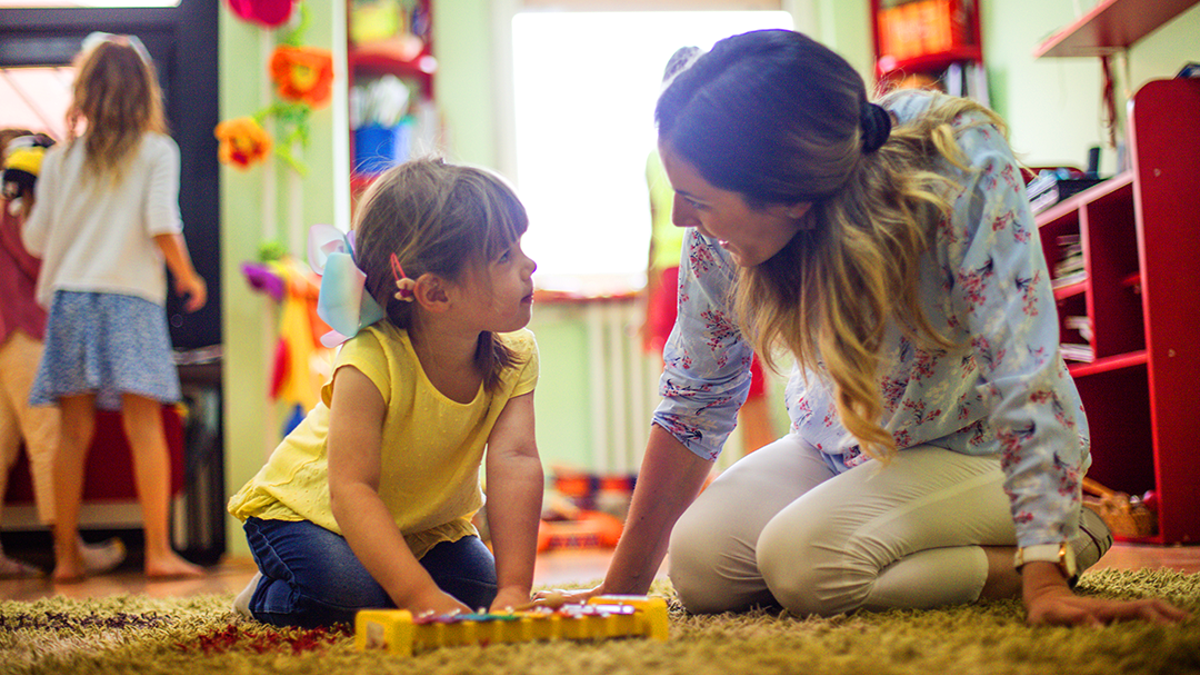 Child and adult playing on a rug the floor with a xylophone.