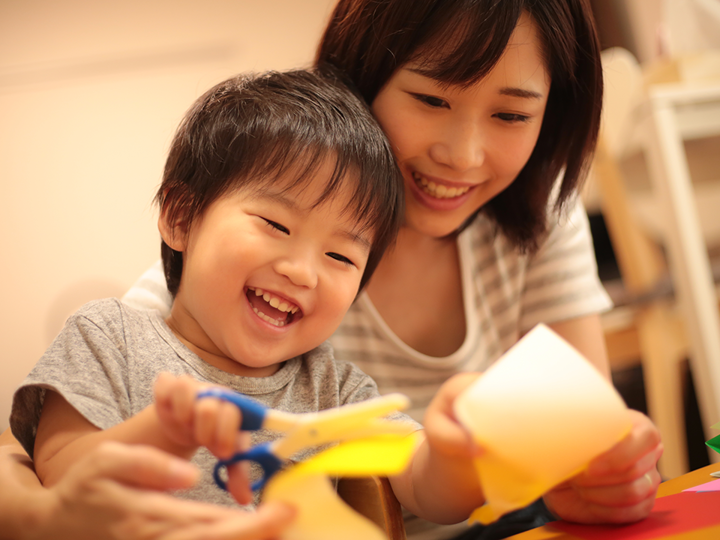 Child sitting on the lap of an adult. Parent is supporting their child cutting paper.