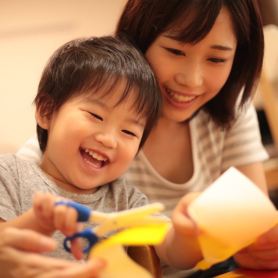 Child sitting on the lap of an adult. Parent is supporting their child cutting paper.