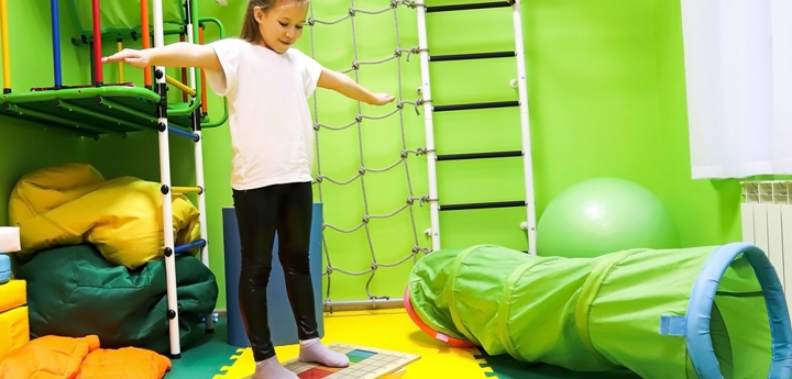 Girl standing on a balance board in a physio room.