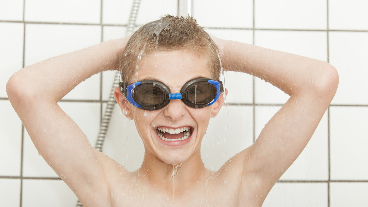 Child standing in a shower, smiling, whilst wearing goggles.