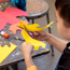 A boy cutting shapes into a yellow piece of paper with scissors.