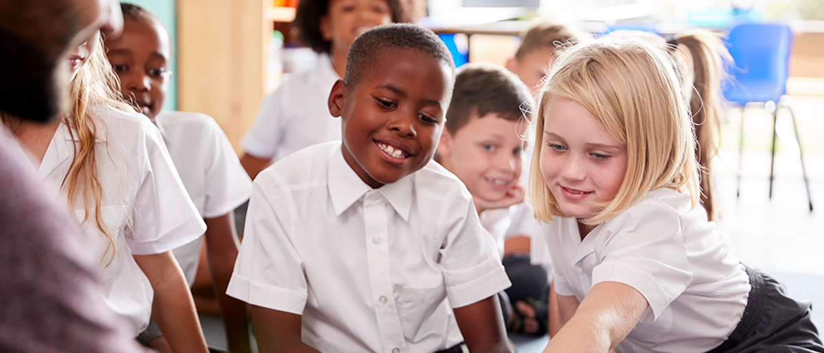 Children in a class looking at a book held by a teacher.