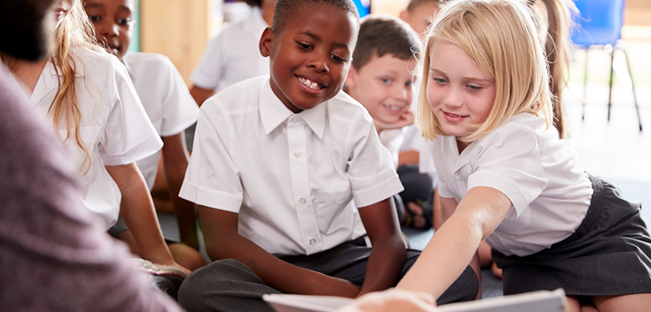 Children in a class looking at a book held by a teacher.