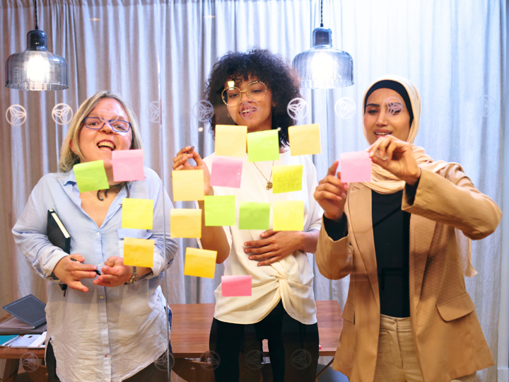 3 smiling women putting Post-It notes on a glass screen