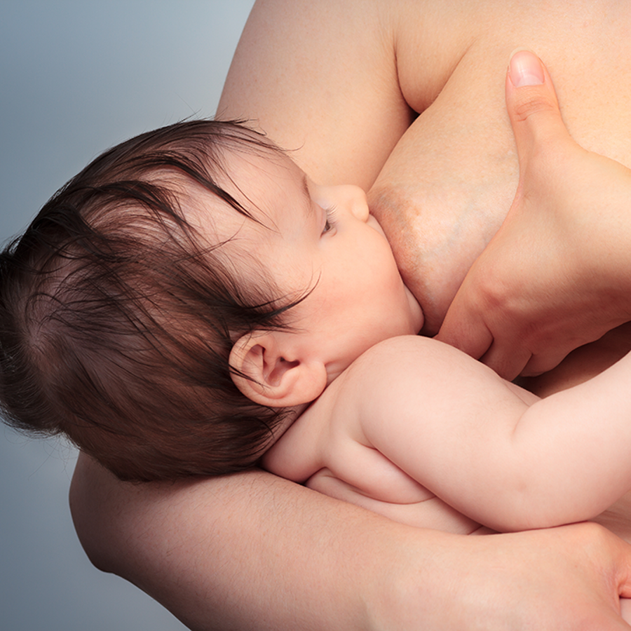 Adult holding their breast whilst breastfeeding their baby.