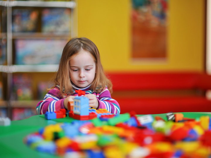 Young girl sat at a green table playing with colourful blocks