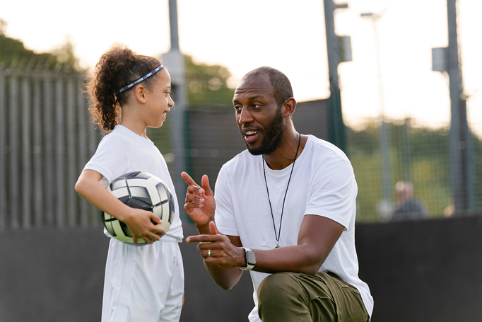 child holding football as adult kneels to give encouragement