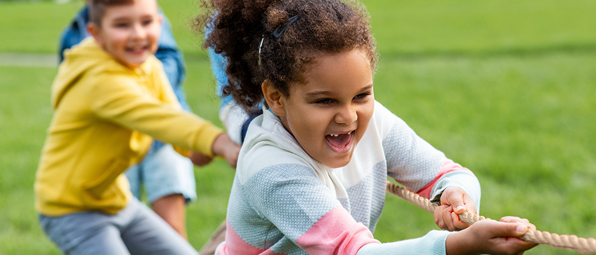 4 children playing tug of war outside in park